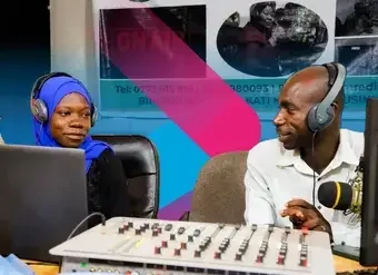 Two radio hosts, a woman and a man, talk in their recording room